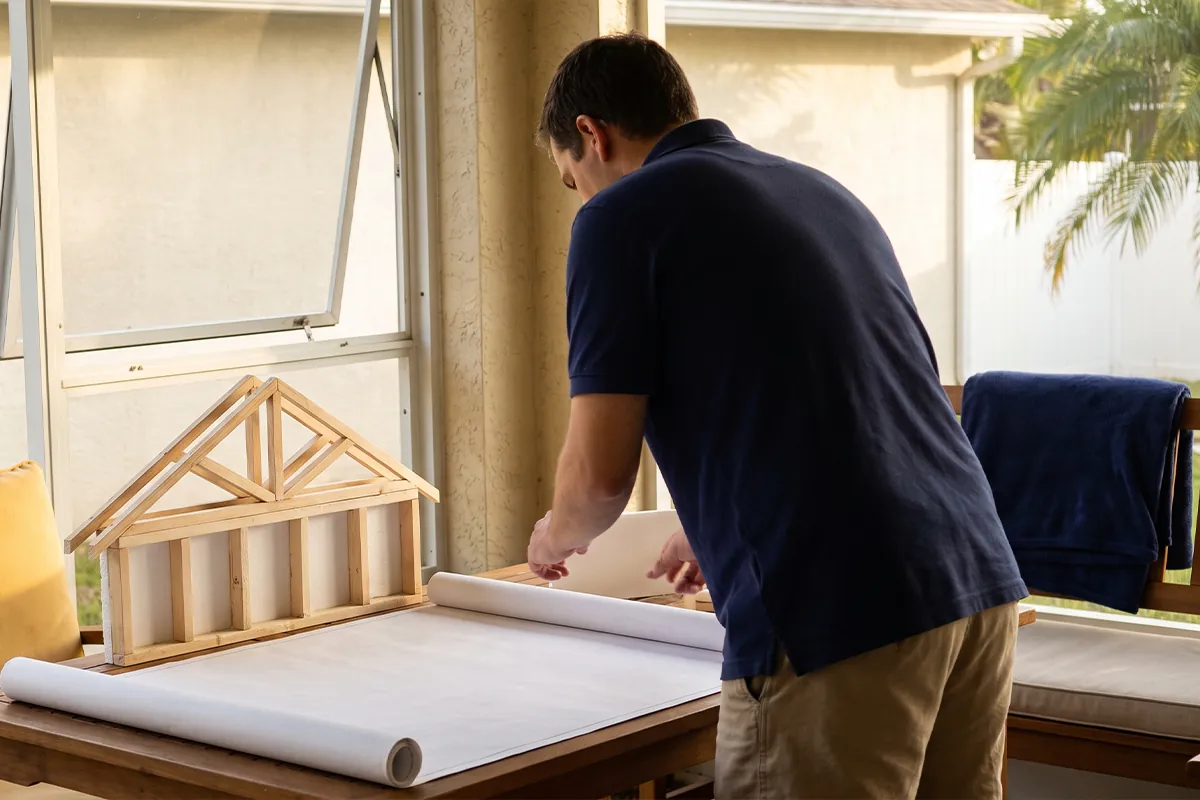 Illustration of a homeowner reviewing a blank plan beside wall and roof cutaways.